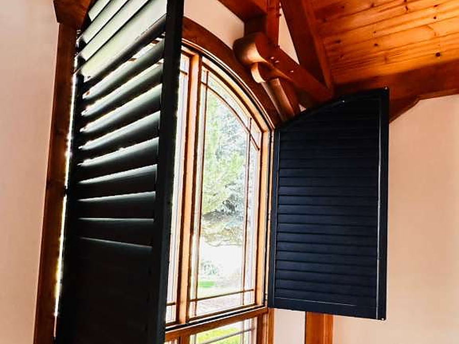 Arched window with black shutters open beneath a vaulted pine ceiling