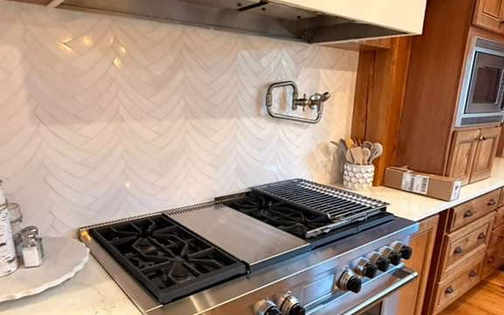 Kitchen with a professional gas range, chevron tile backsplash and quartz counters cleaned