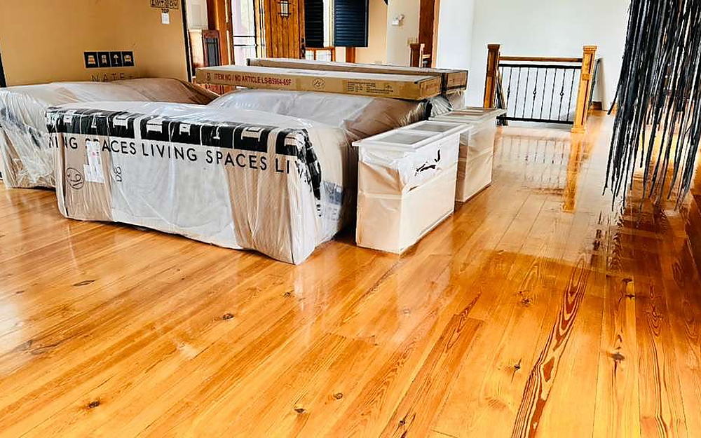 Living area with plastic-wrapped furniture on a polished pine floor during a move-in clean