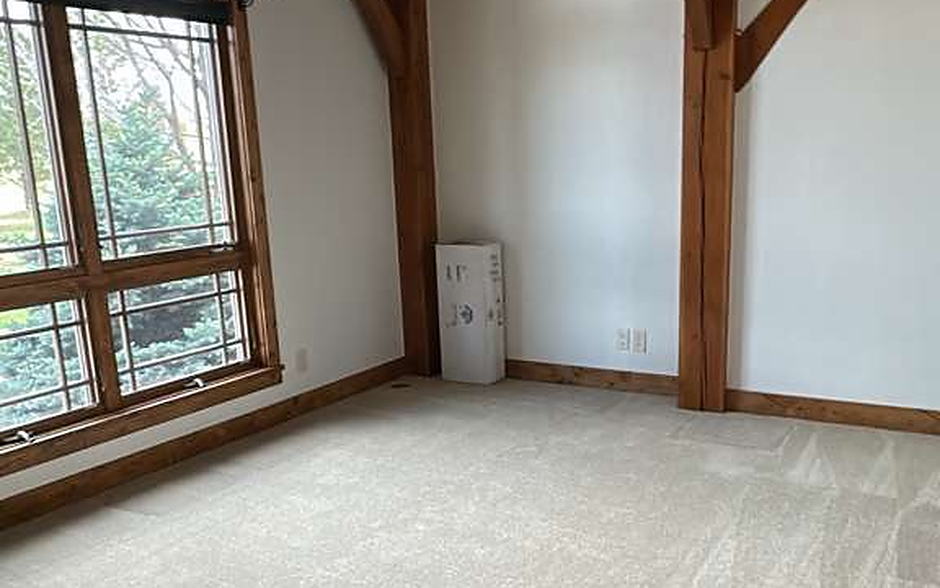 Empty carpeted room with an arched window and exposed timber truss