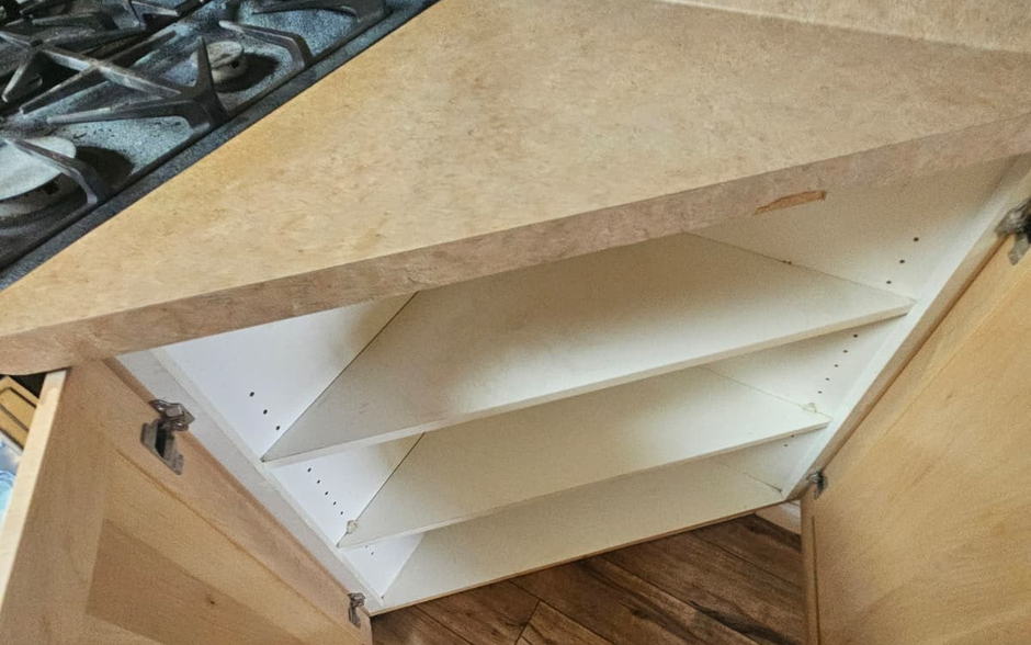 Empty corner base cabinet with bare shelves beside a gas range, cleaned inside on a move-out visit