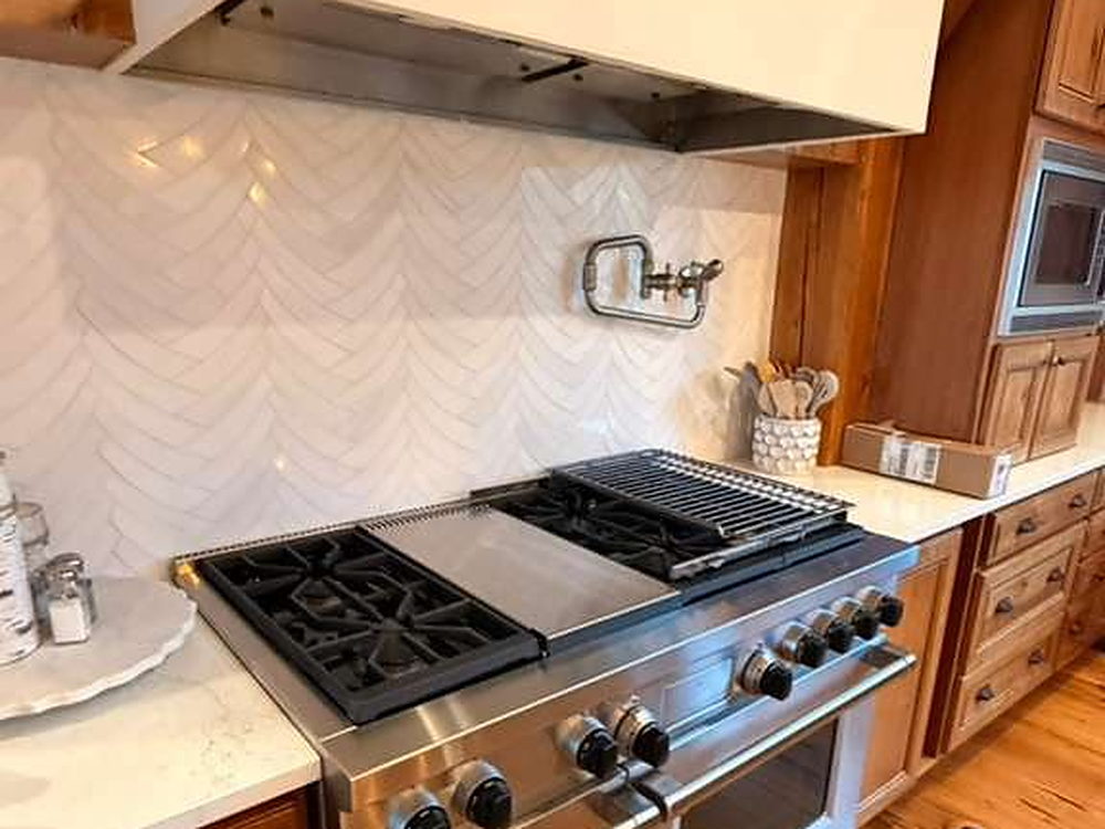 Kitchen with a professional gas range, chevron tile backsplash and quartz counters cleaned