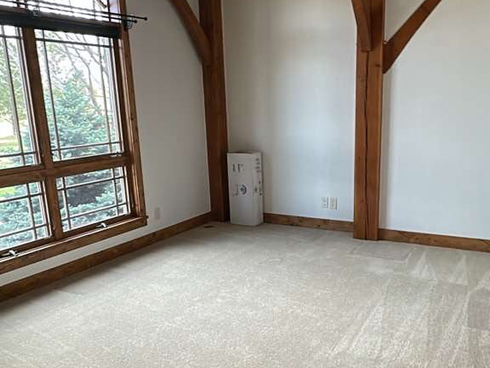 Empty carpeted room with an arched window and exposed timber truss