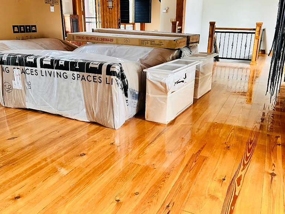 Living area with plastic-wrapped furniture on a polished pine floor during a move-in clean