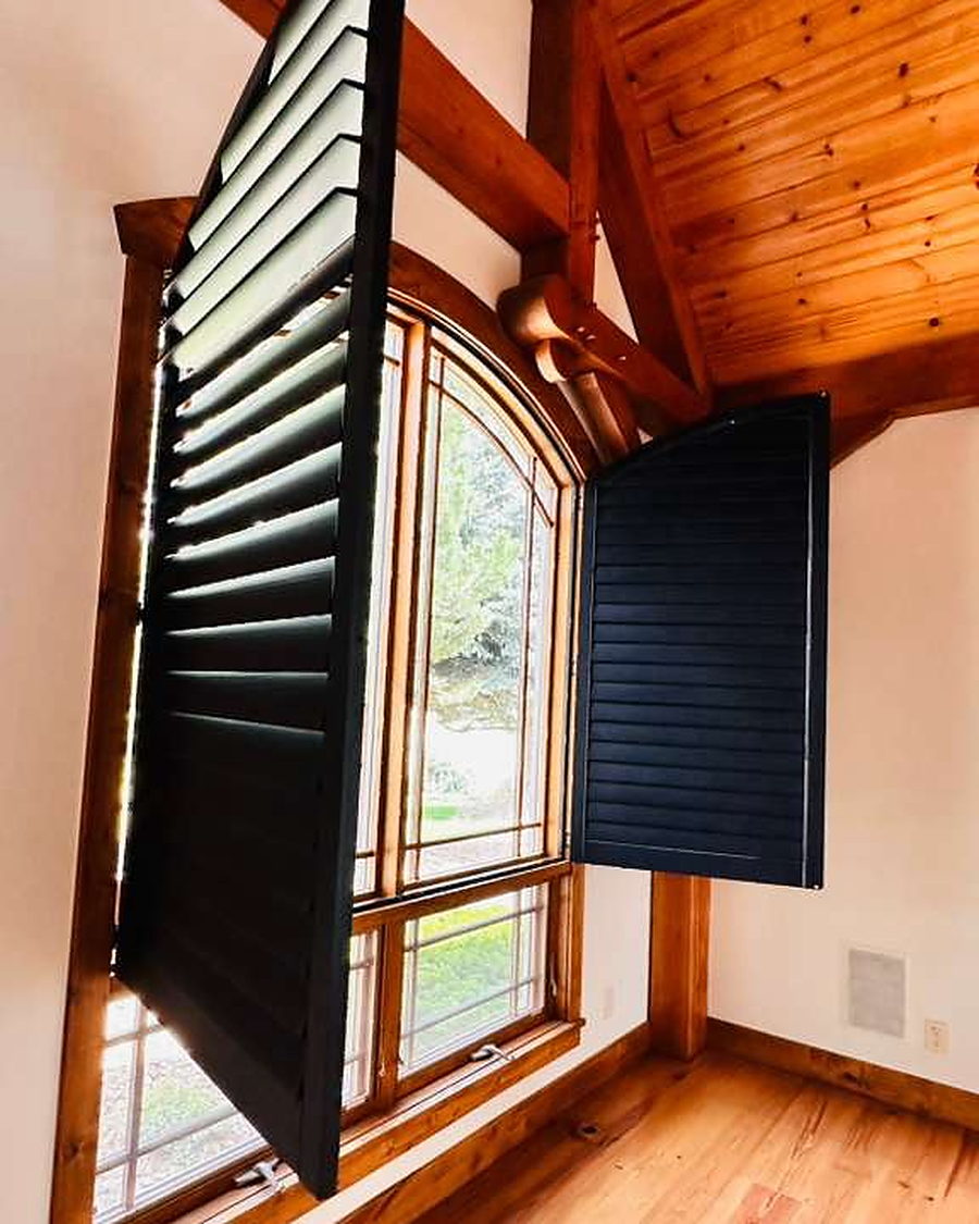 Arched window with black shutters open beneath a vaulted pine ceiling