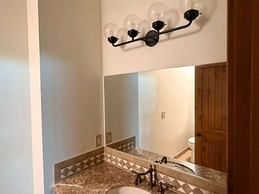 Bathroom vanity with granite counter, mirror and black sconce lighting cleaned