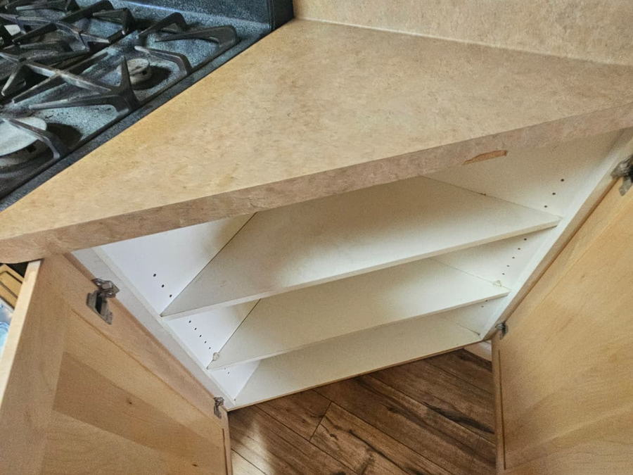 Empty corner base cabinet with bare shelves beside a gas range, cleaned inside on a move-out visit